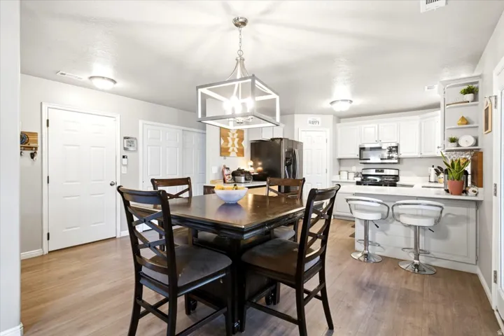 Kitchen featuring wood-finish flooring, white cabinetry, integrated stainless steel appliances, and a central pendant light fixture
