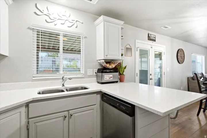 White shaker-style cabinetry, stainless steel double basin sink, light-toned countertops, integrated dishwasher, and wood-finish flooring