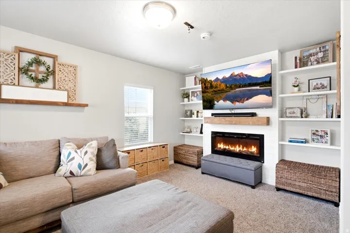 Built-in shelving, electric fireplace with a wood-finish mantel, and carpeted flooring
