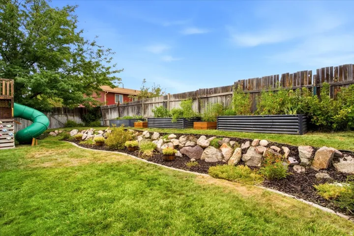 Expansive backyard featuring a lush lawn, a rock-lined garden bed, and corrugated metal raised garden beds