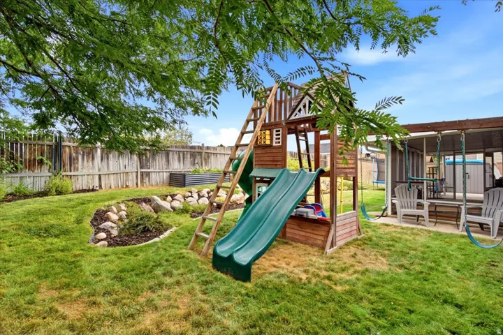 Expansive backyard featuring a manicured lawn, established landscaping, and a covered patio area