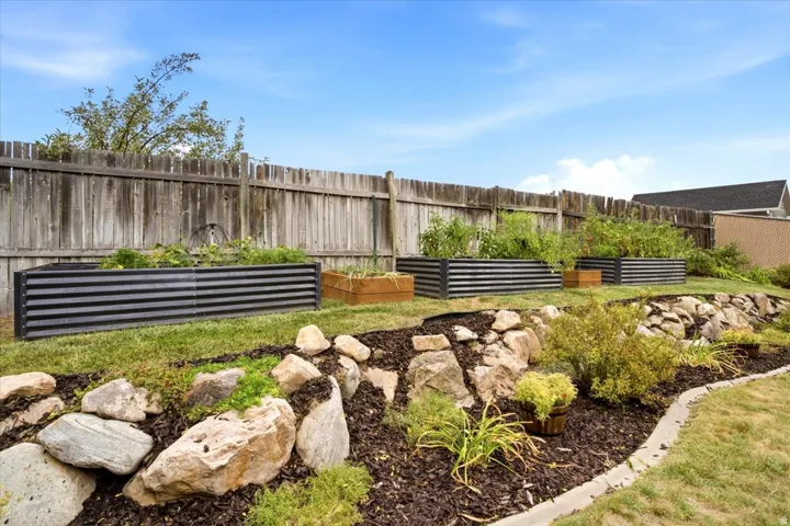 Expansive backyard featuring a natural wood fence, multiple raised garden beds, a rock retaining wall, and landscaped planting areas