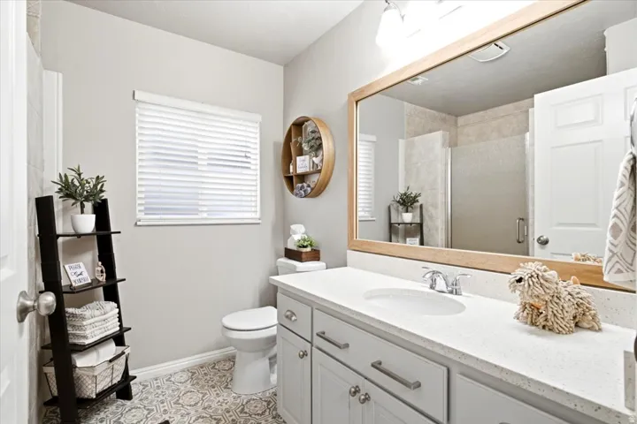 Bathroom featuring a single vanity with light-toned countertop, wood-framed mirror, and patterned floor tile