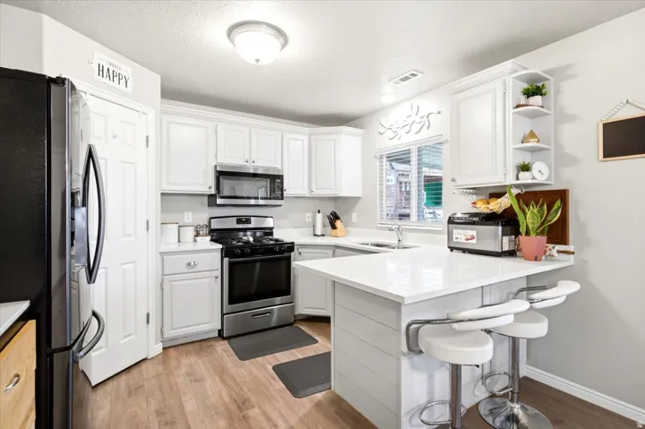 White cabinetry with stainless steel appliances, wood-finish flooring, white countertops, and a kitchen island with seating