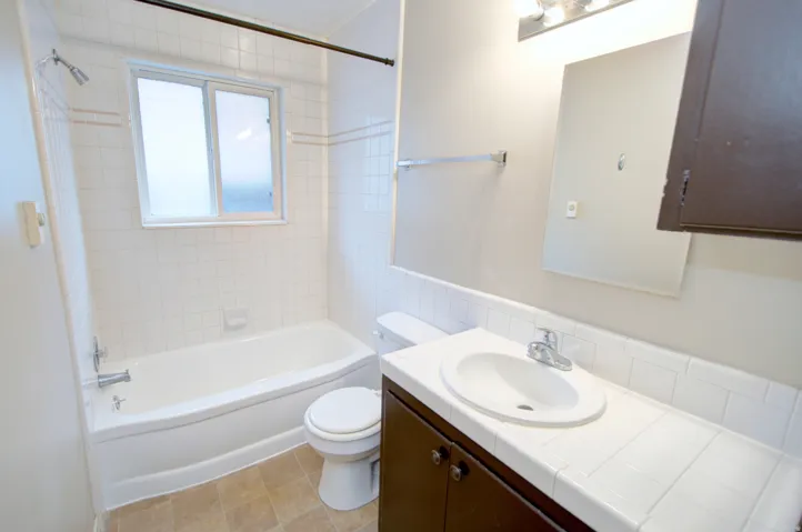 Bathroom featuring a white bathtub, tiled shower surround, frosted window, vanity with integrated sink, and a mirrored medicine cabinet