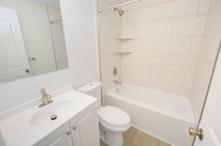 Bathroom featuring a white vanity with integrated sink, brushed nickel faucet, a toilet, and a white bathtub with subway tile surround and integrated shelving