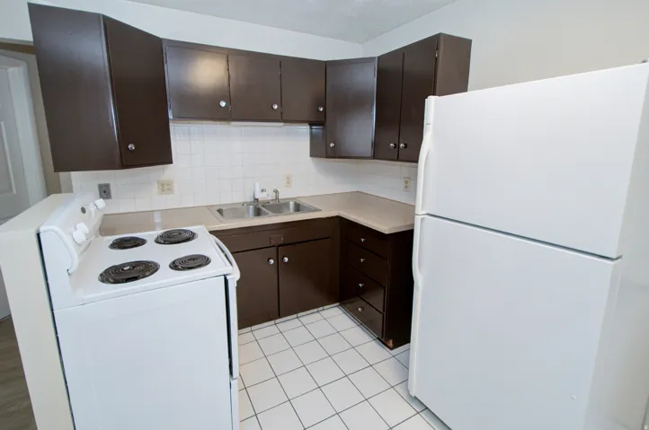 White tile flooring, brown cabinetry, light-toned countertops, white electric range, and white refrigerator