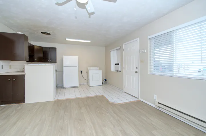 Open-concept living area featuring wood-finish flooring, a kitchen with dark cabinetry and white tile backsplash, and a dedicated laundry area with tile flooring