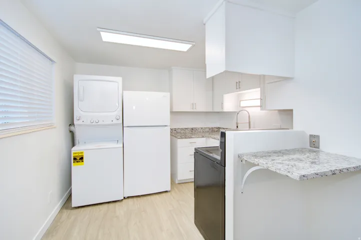White stacked washer and dryer, white refrigerator, wood-finish flooring, white cabinetry, and light-toned countertop