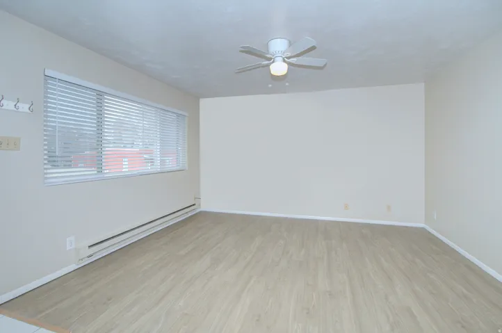 Wood-finish flooring, white walls, white window blinds, and a ceiling fan with integrated lighting