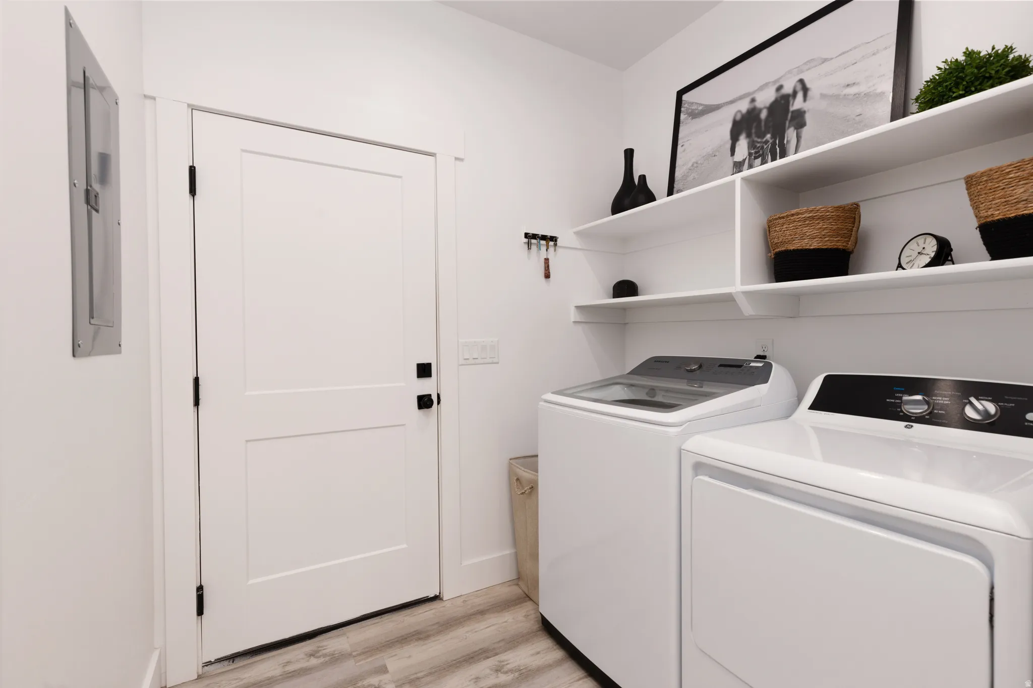 Dedicated laundry area featuring a washer and dryer, open white shelving, and wood-finish flooring