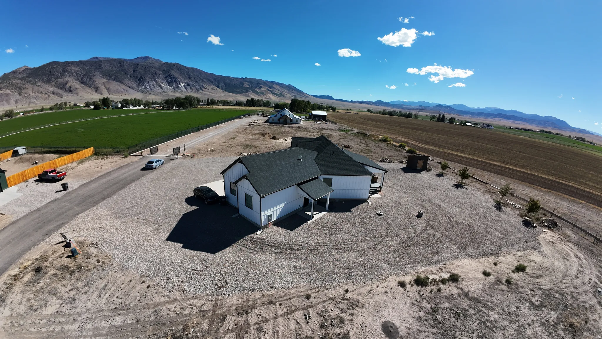 White exterior siding, dark roof, gravel landscaping, mountain backdrop, and expansive open fields
