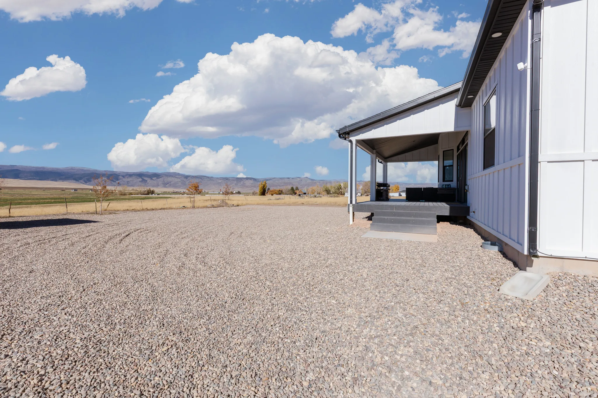 White vertical siding, covered patio, dark gray porch steps, gravel landscaping, and distant mountain scenery