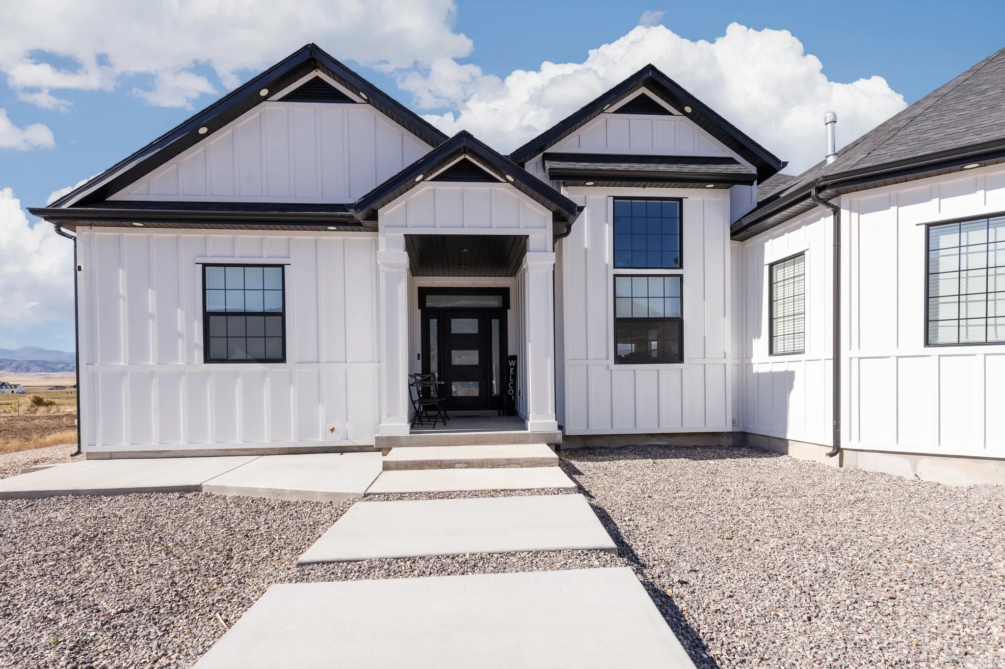 Modern farmhouse exterior featuring white board and batten siding, black trim, a dark asphalt shingle roof, and multiple large grid windows