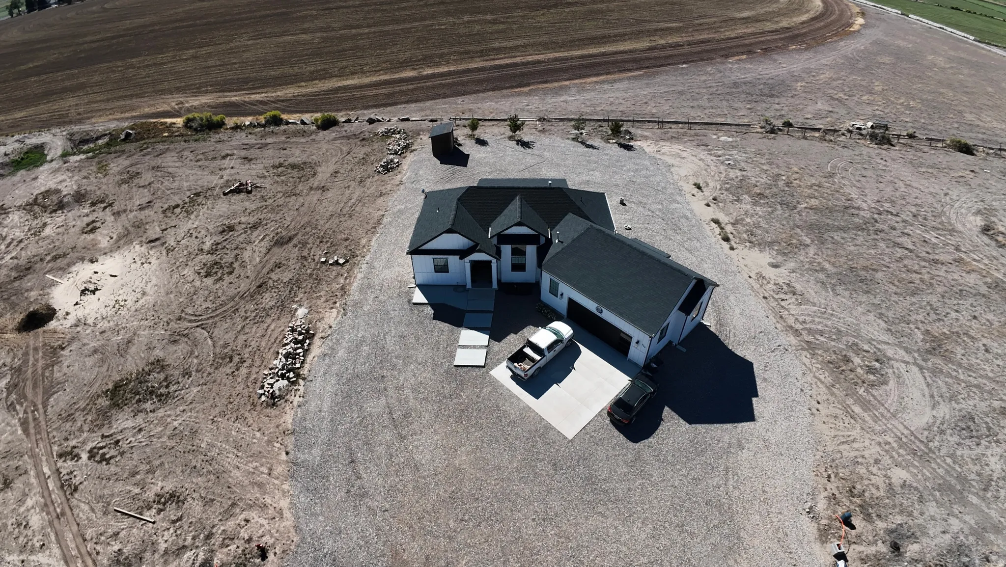 Newly constructed residence featuring a dark shingle roof, light-colored siding, an attached garage, and a gravel driveway
