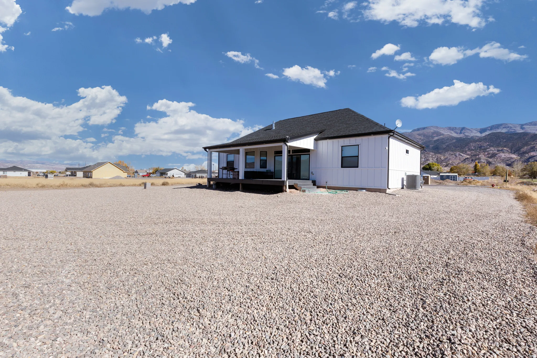 White siding with dark trim, dark shingle roof, expansive gravel lot, covered deck