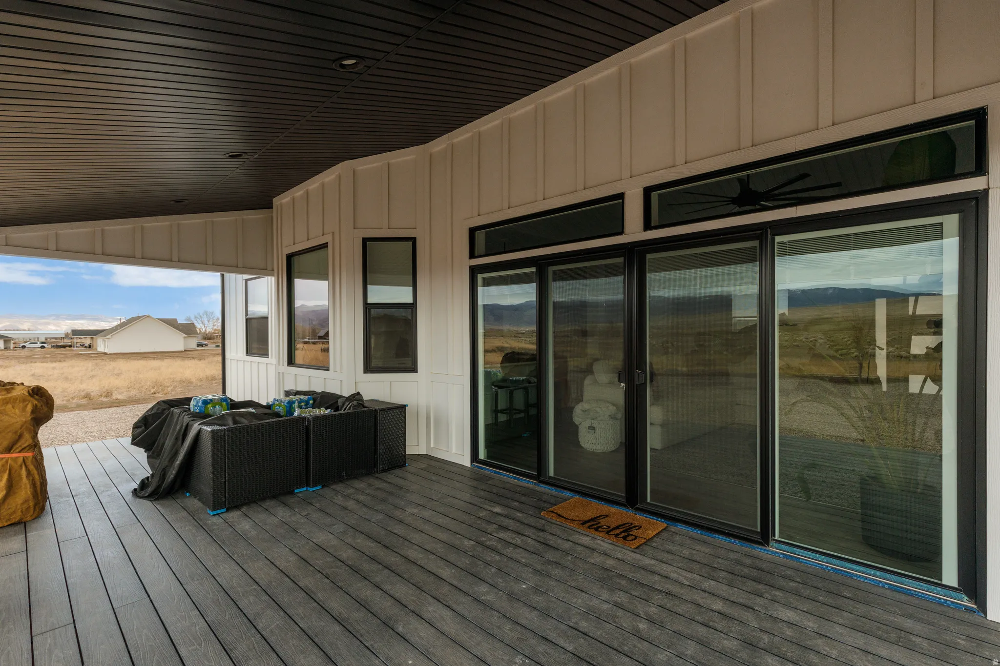 Covered exterior porch featuring composite decking, board and batten siding, black-framed sliding glass doors, and a dark-paneled ceiling