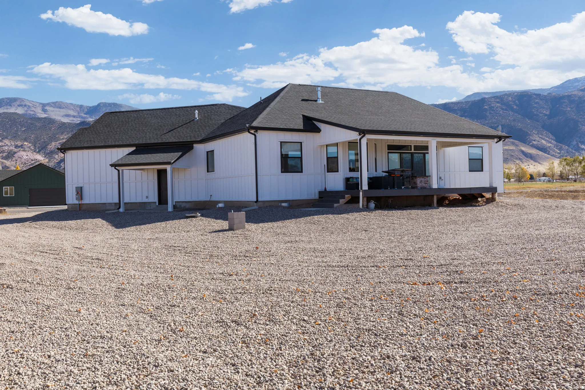 White board and batten siding, dark shingle roof, covered patio with wood decking, and a covered entry