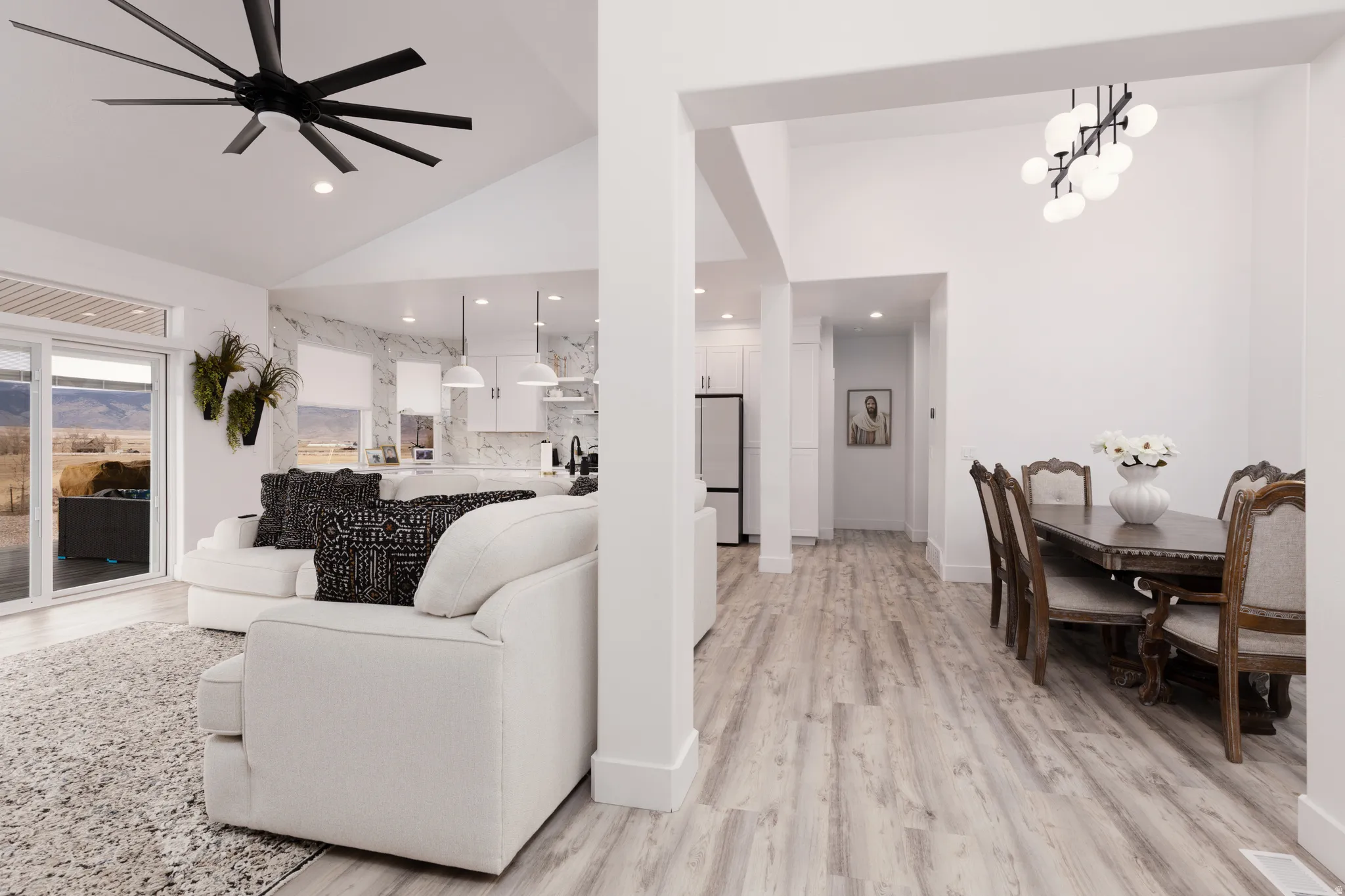 Vaulted ceiling with a black multi-blade ceiling fan, wood-finish flooring, and white walls
