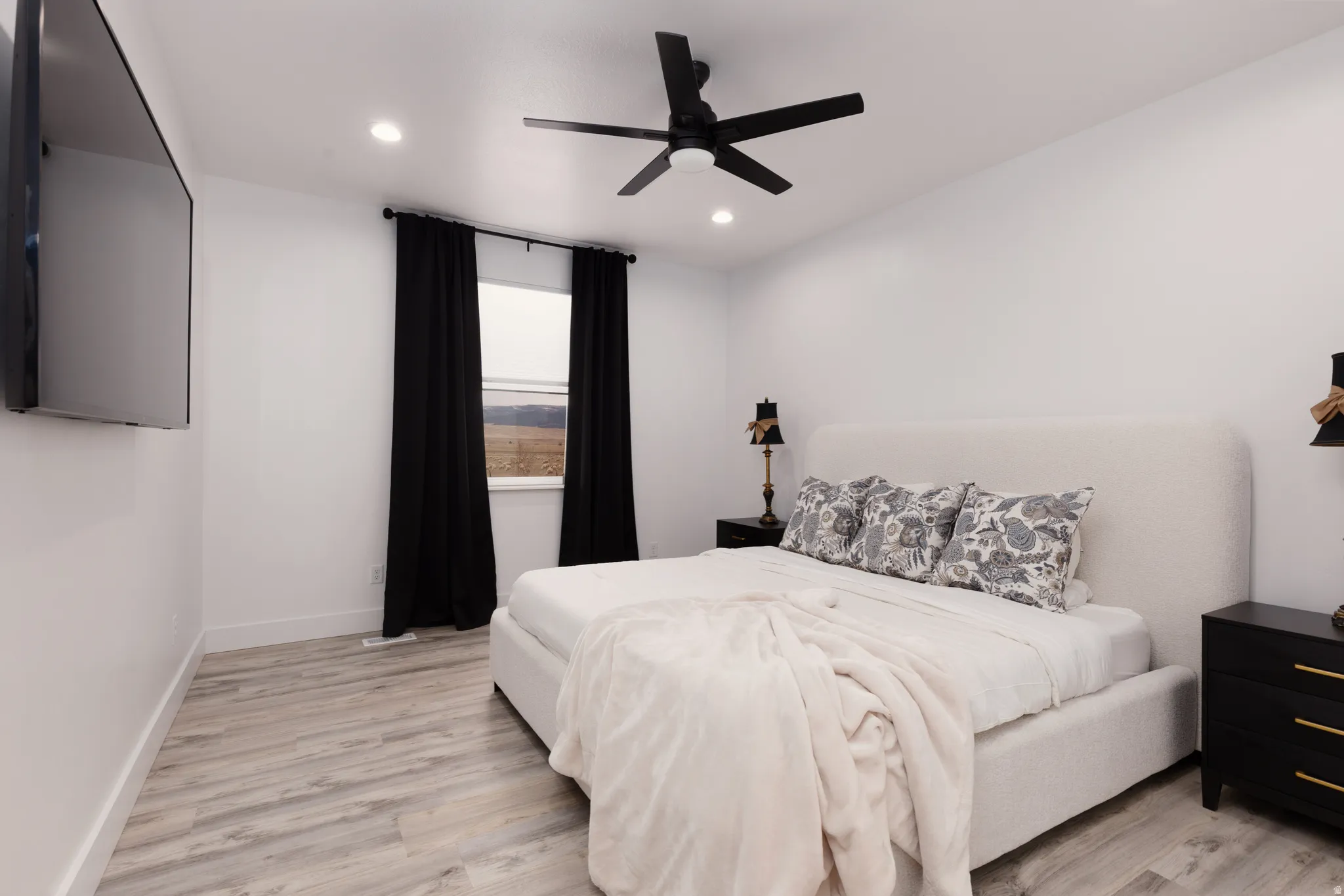 Wood-finish flooring, recessed lighting, ceiling fan, and a single window with dark drapes