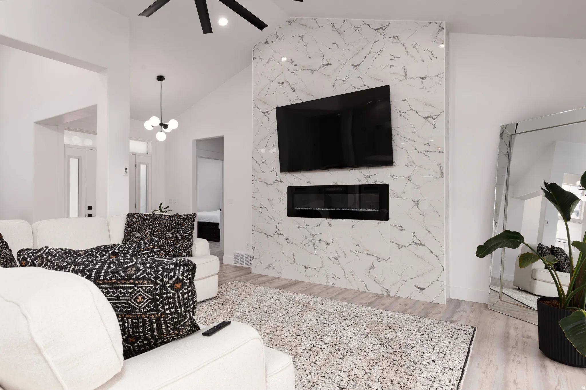 Vaulted ceiling with a black ceiling fan, wood-finish flooring, and a decorative chandelier
