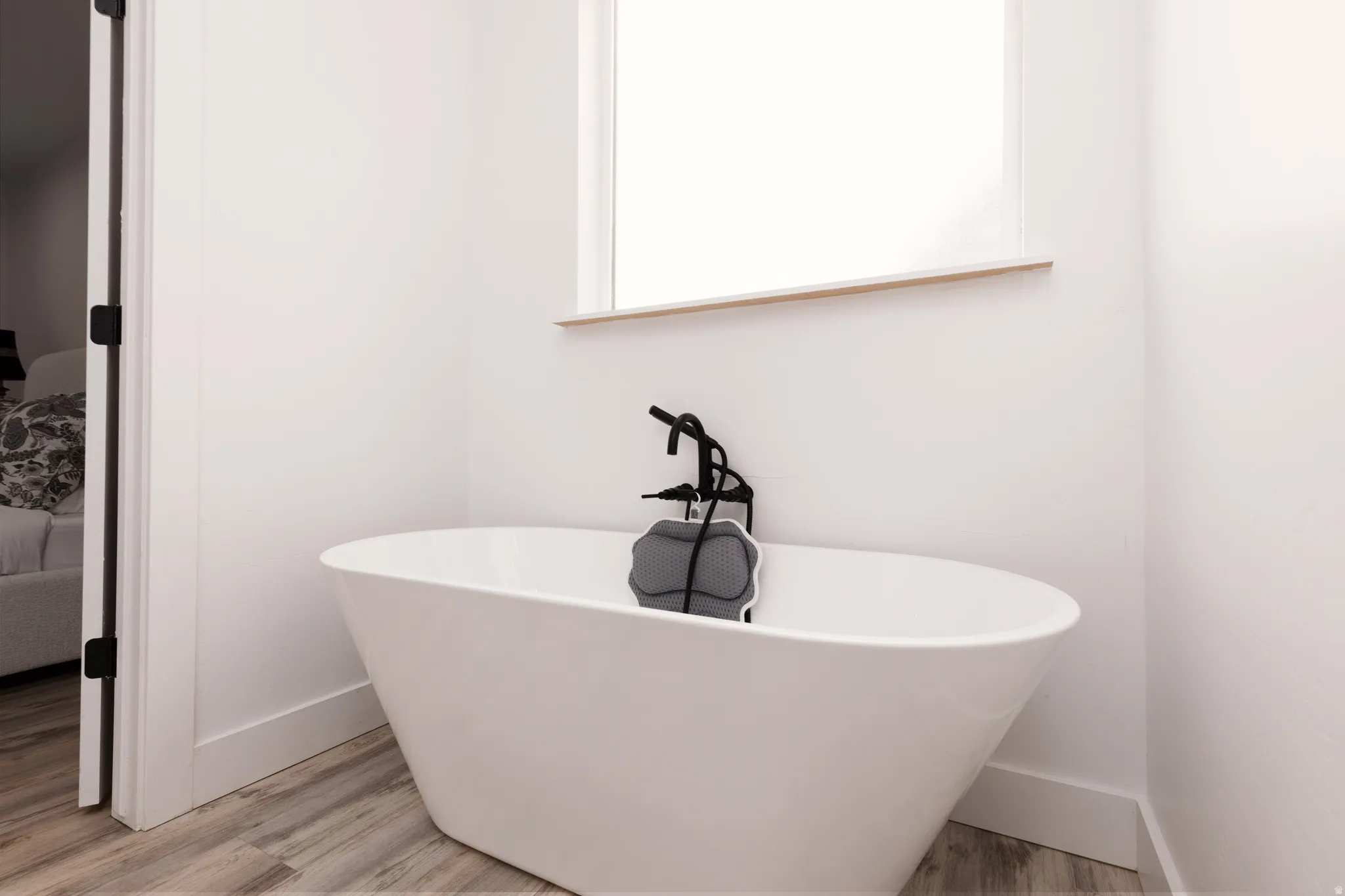 Freestanding soaking tub with a matte black floor-mounted faucet, wood-finish flooring, and white walls