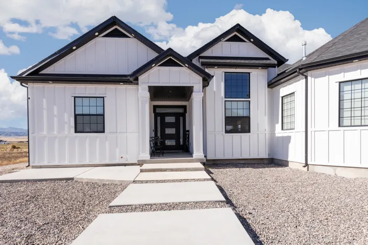 Modern farmhouse exterior featuring white board and batten siding, black trim, a dark asphalt shingle roof, and multiple large grid windows