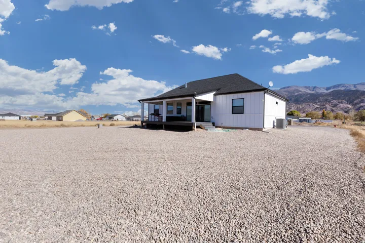White siding with dark trim, dark shingle roof, expansive gravel lot, covered deck
