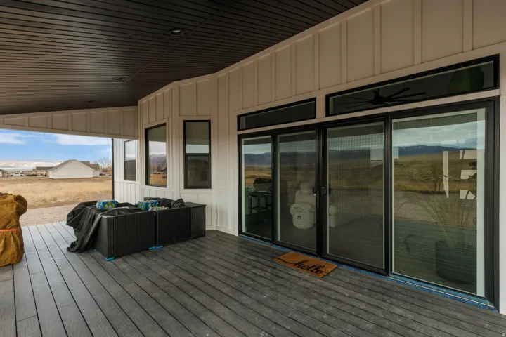 Covered exterior porch featuring composite decking, board and batten siding, black-framed sliding glass doors, and a dark-paneled ceiling