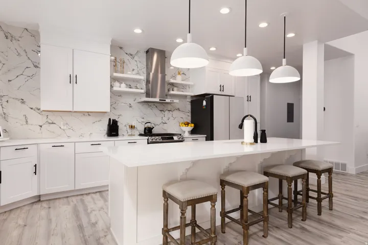 White cabinetry, patterned backsplash, stainless steel range hood, white island with seating, and light wood-finish flooring