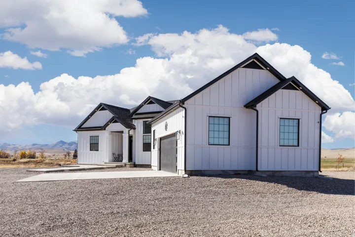 White vertical siding exterior with black trim, multiple gables, attached garage, covered entry, and gravel driveway
