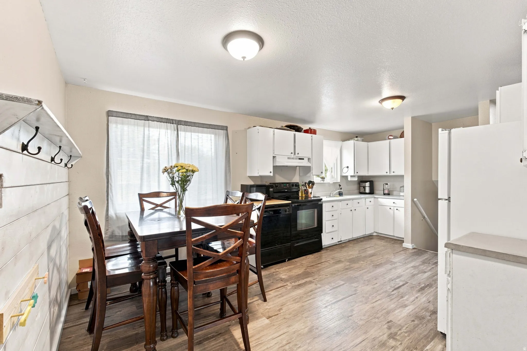 Kitchen featuring white cabinetry, black appliances, light-toned countertops, and wood-finish flooring