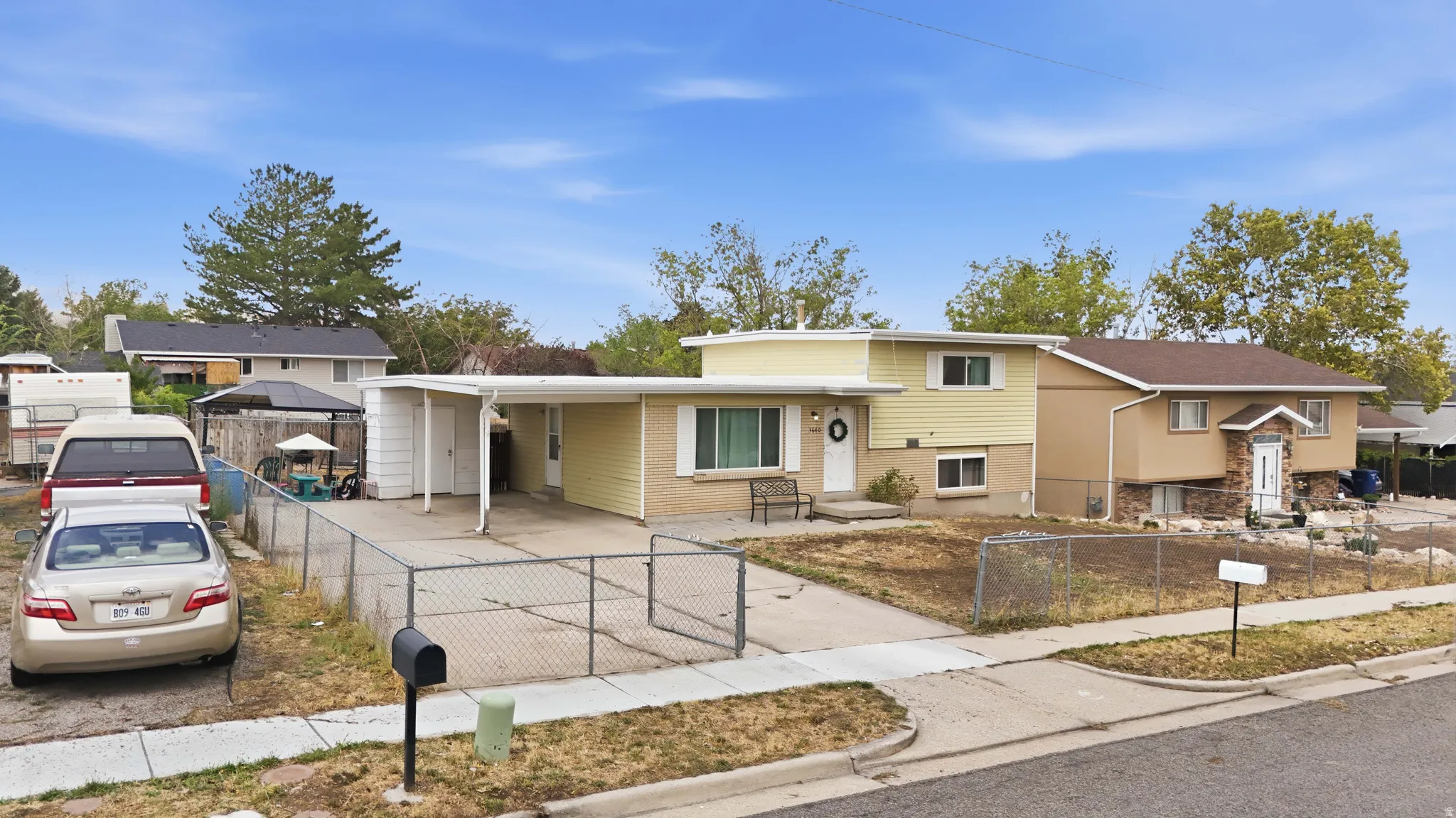 Single-story residence featuring a carport, a paved driveway, and a chain-link fence