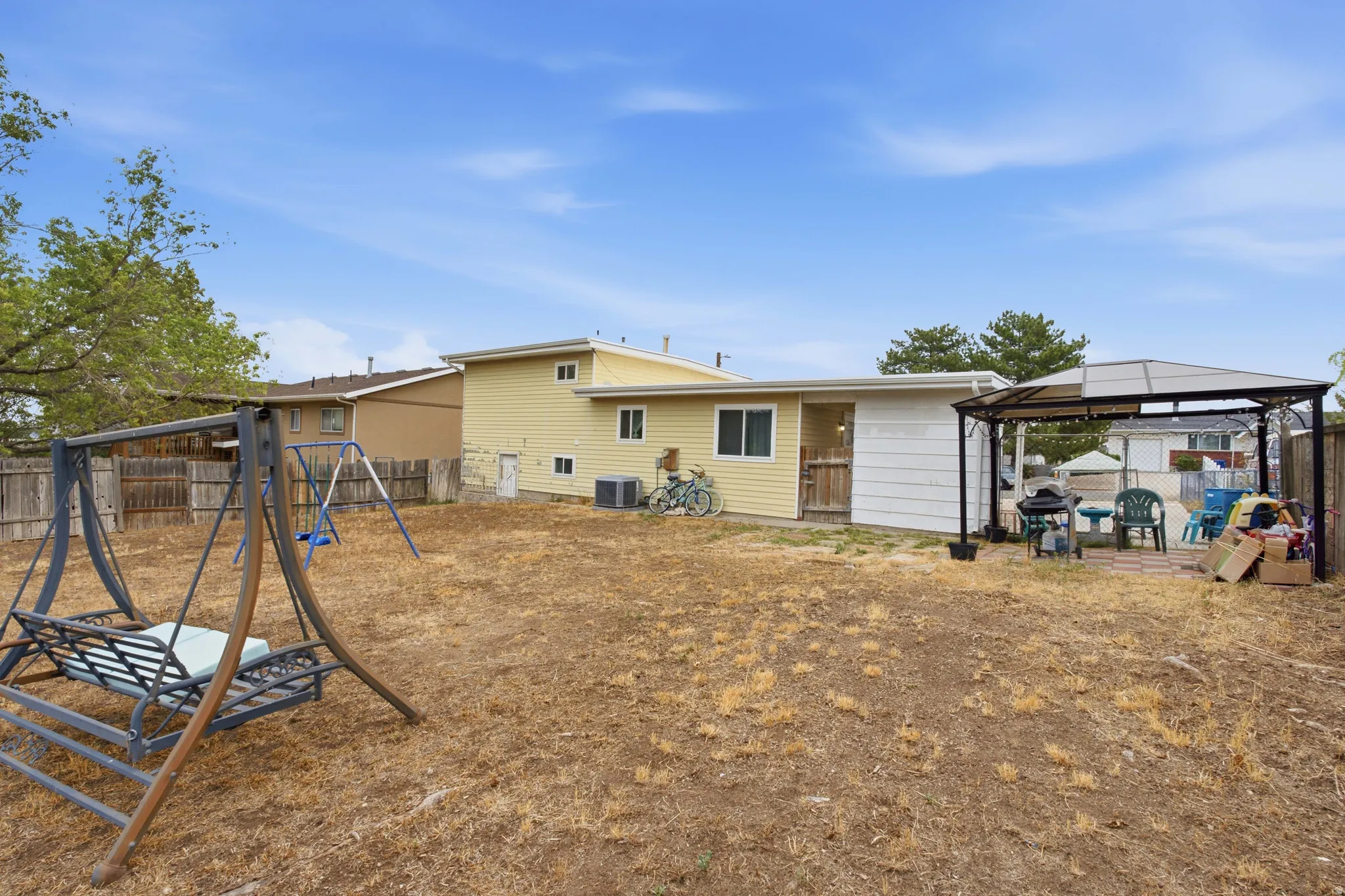 Spacious backyard with mature landscaping and established trees, equipped with a swing set and covered patio area
