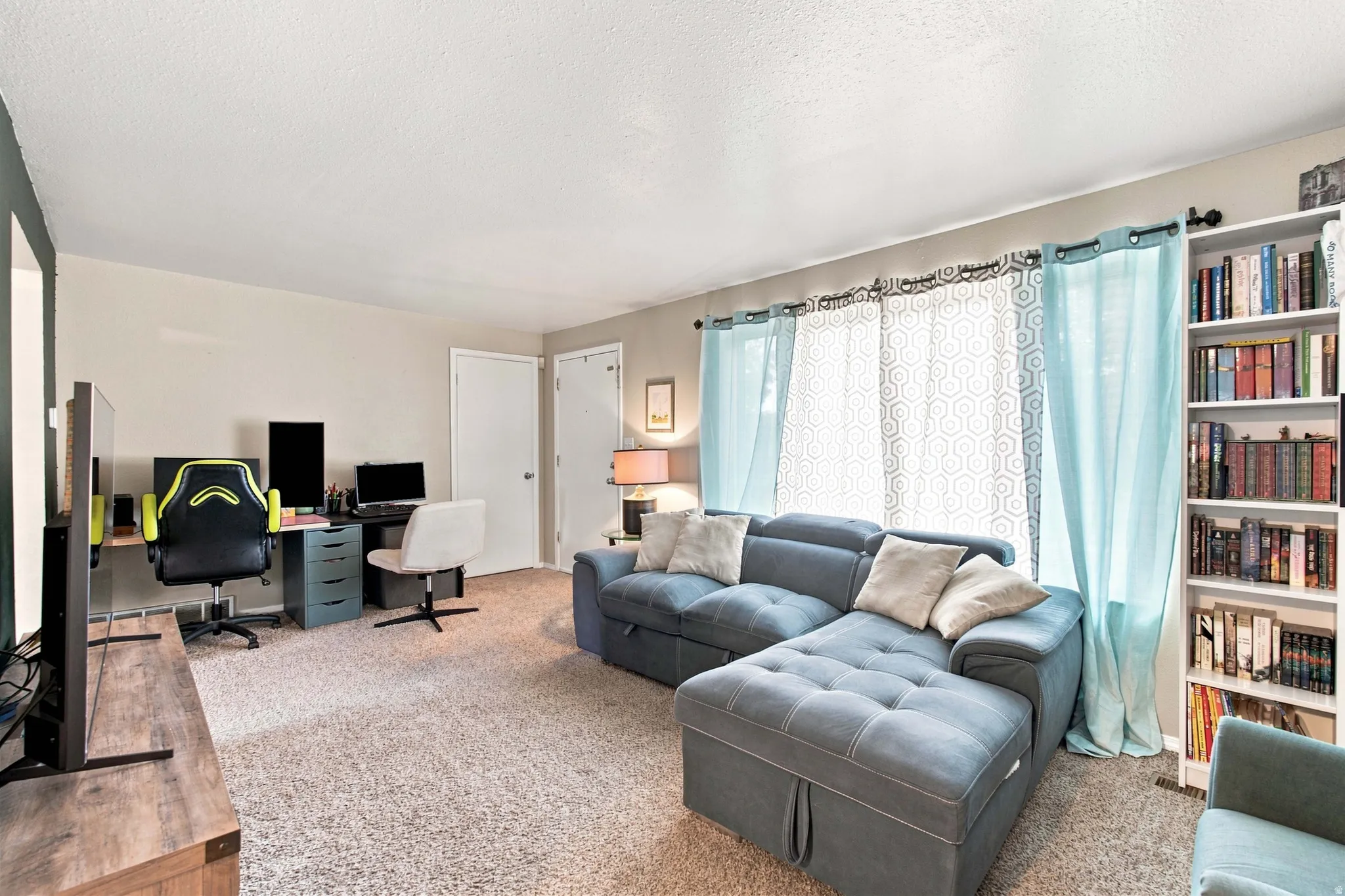 Carpeted common area featuring a built-in bookshelf, dual doors, and curtained windows