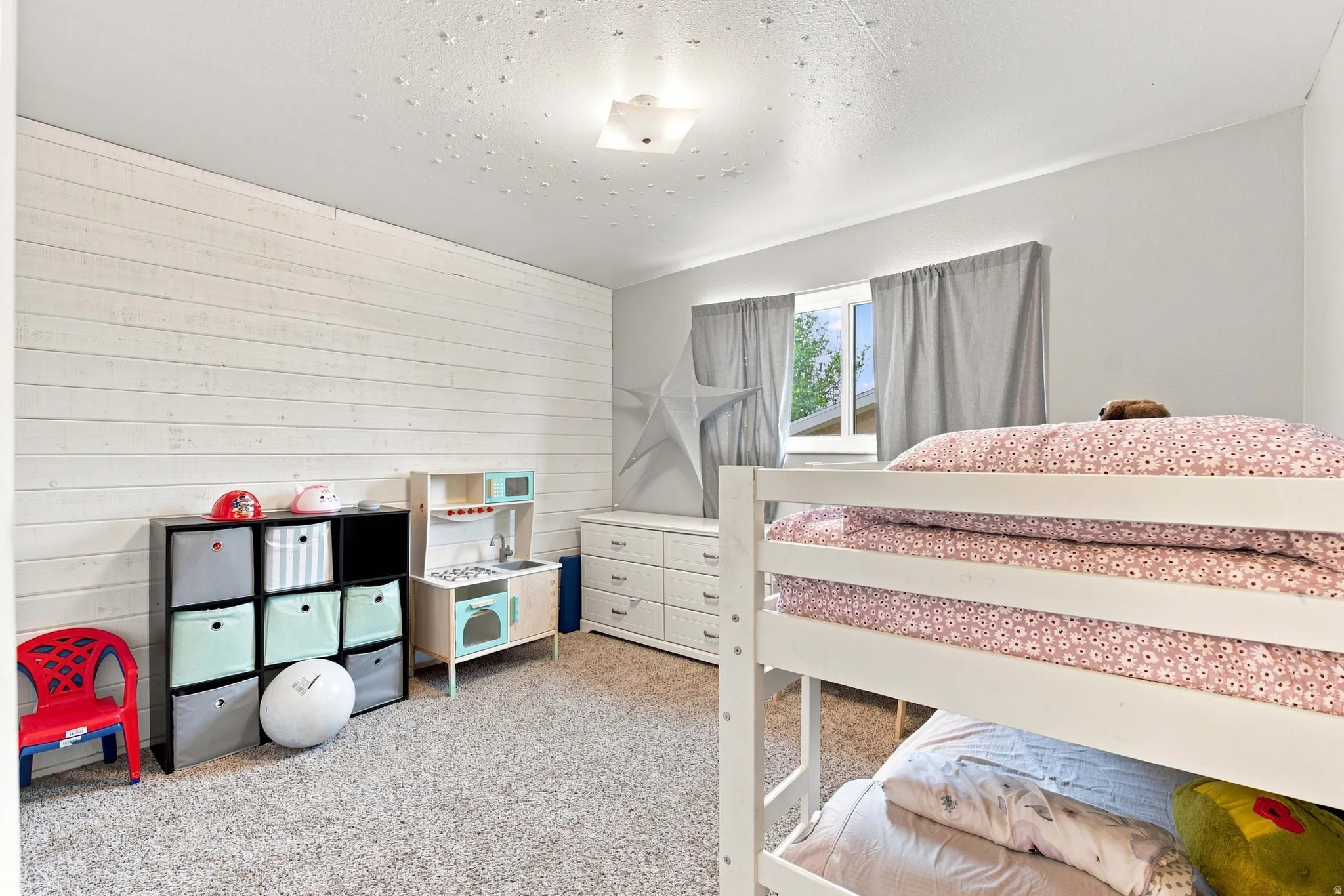 Light-colored carpeted flooring, window with natural light, white shiplap-style accent wall, and a flush-mount ceiling light fixture