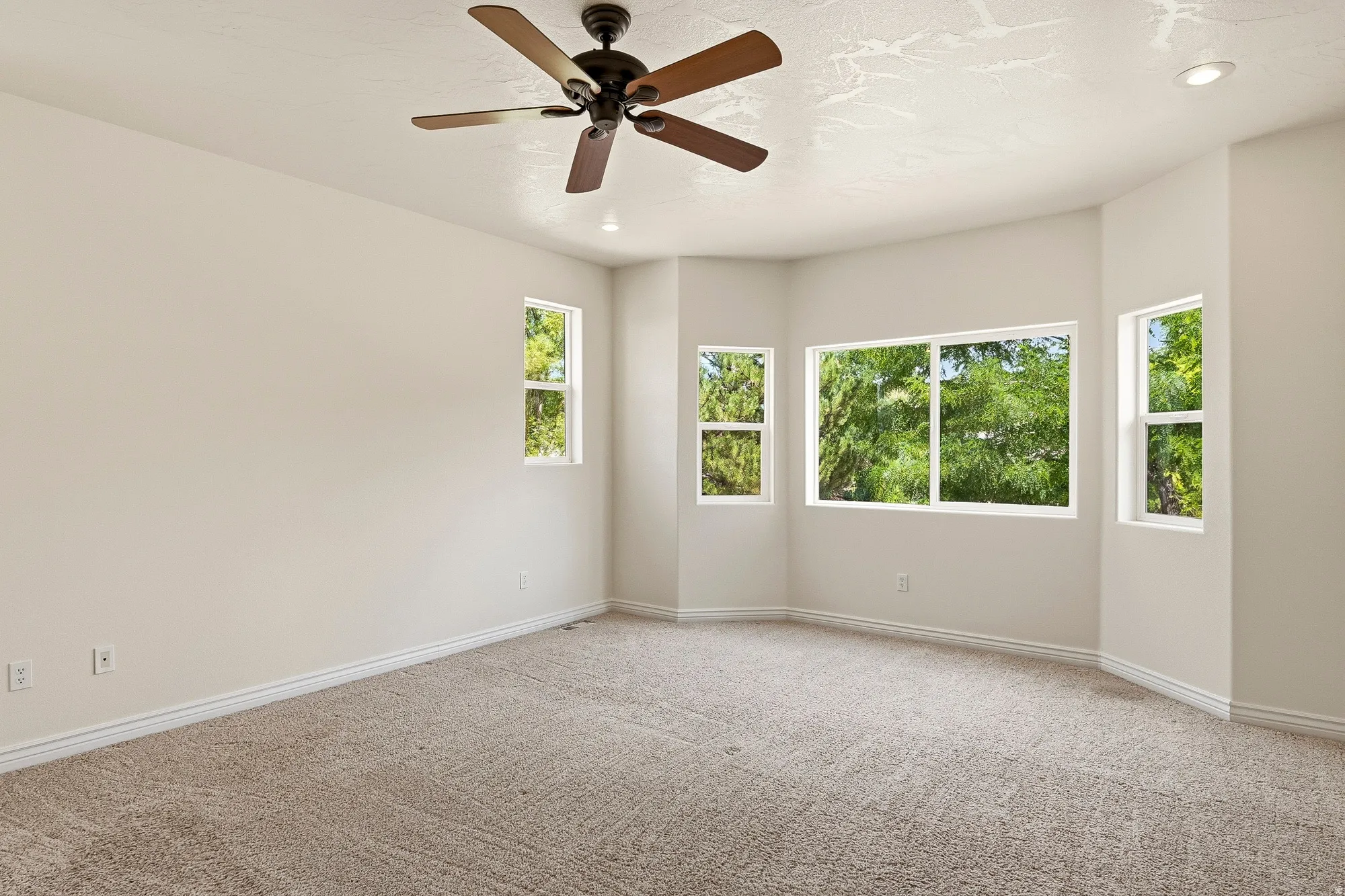 Carpeted room featuring a ceiling fan, recessed lighting, and multiple windows