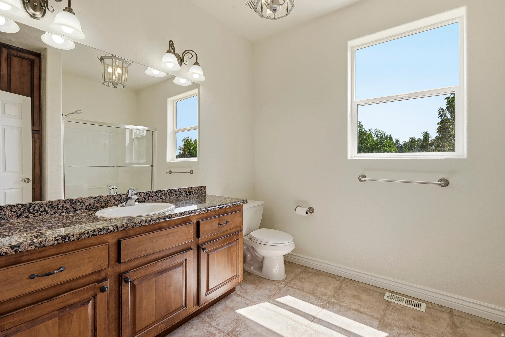 Wood-finish vanity with an undermount sink and granite-style countertop, complemented by a large wall mirror