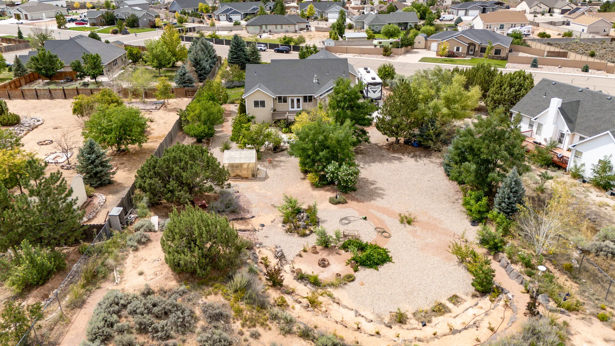 Expansive property featuring mature trees, diverse plantings, and a gravel-covered yard