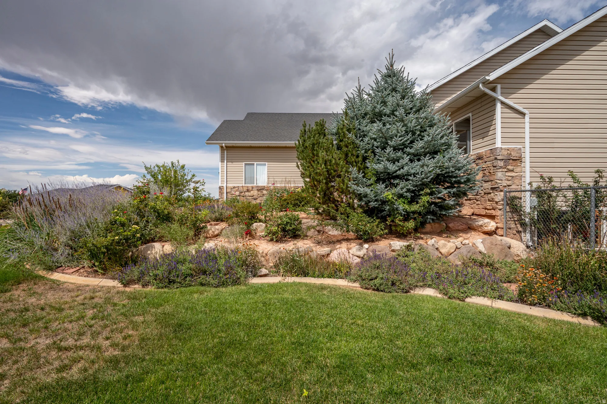 Manicured lawn with a stone and rock retaining wall, mature evergreen trees, and established landscaping