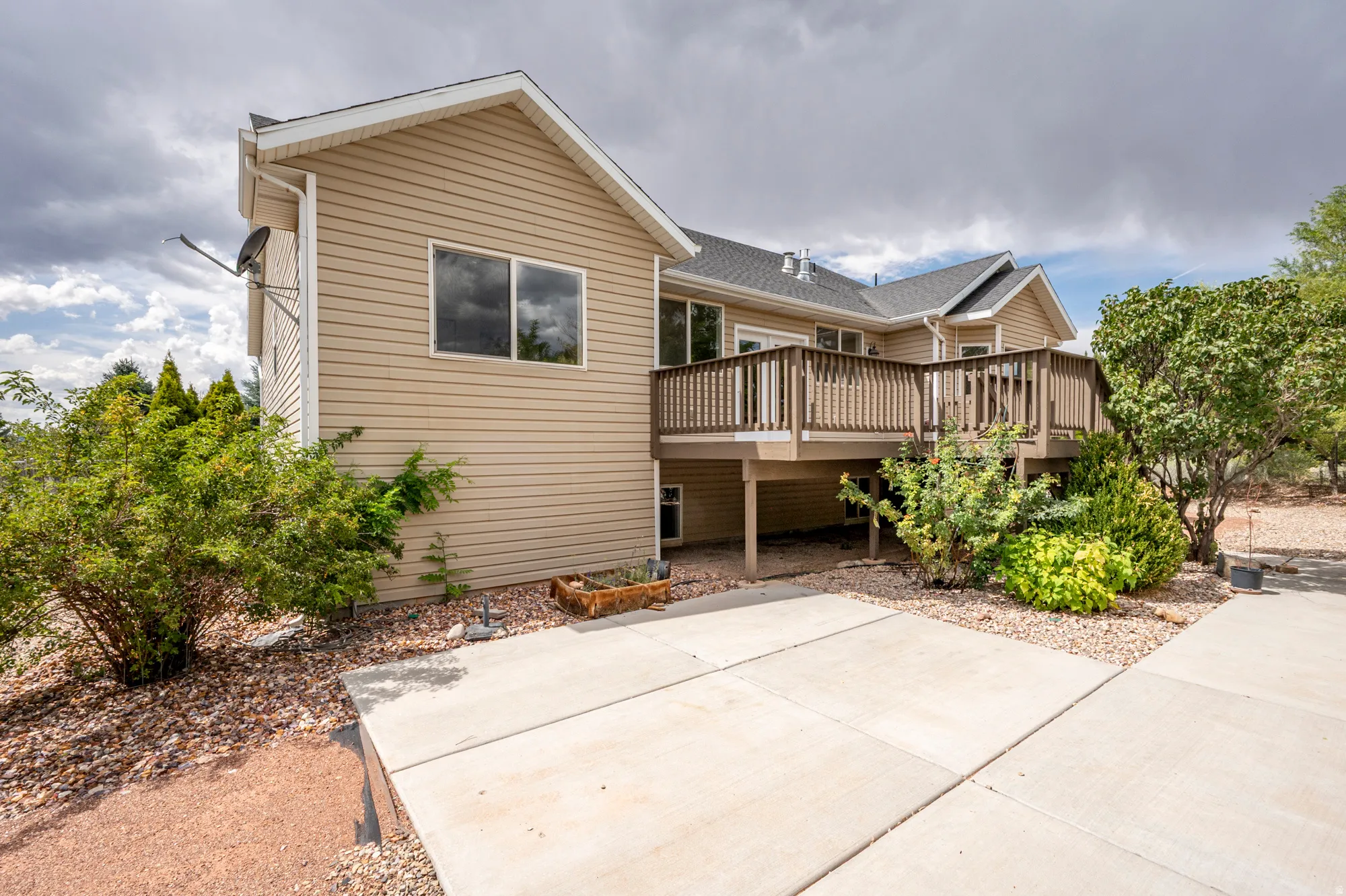 Expansive rear deck with wood railing, tan siding exterior, multiple windows, and a concrete patio below