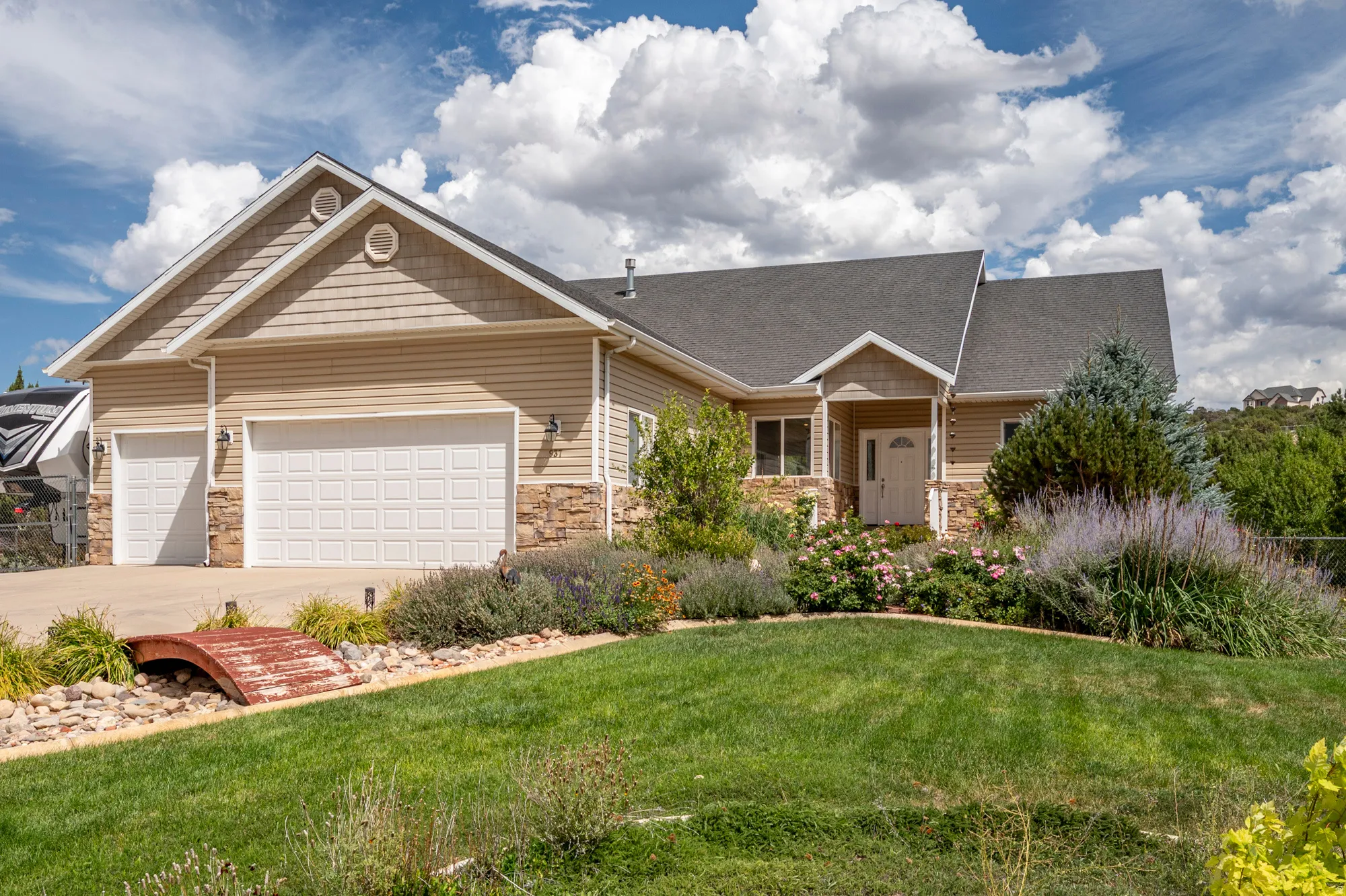 Exterior featuring horizontal siding, stone facade accents, a dark shingle roof, attached two-car garage, and a manicured lawn with mature landscaping