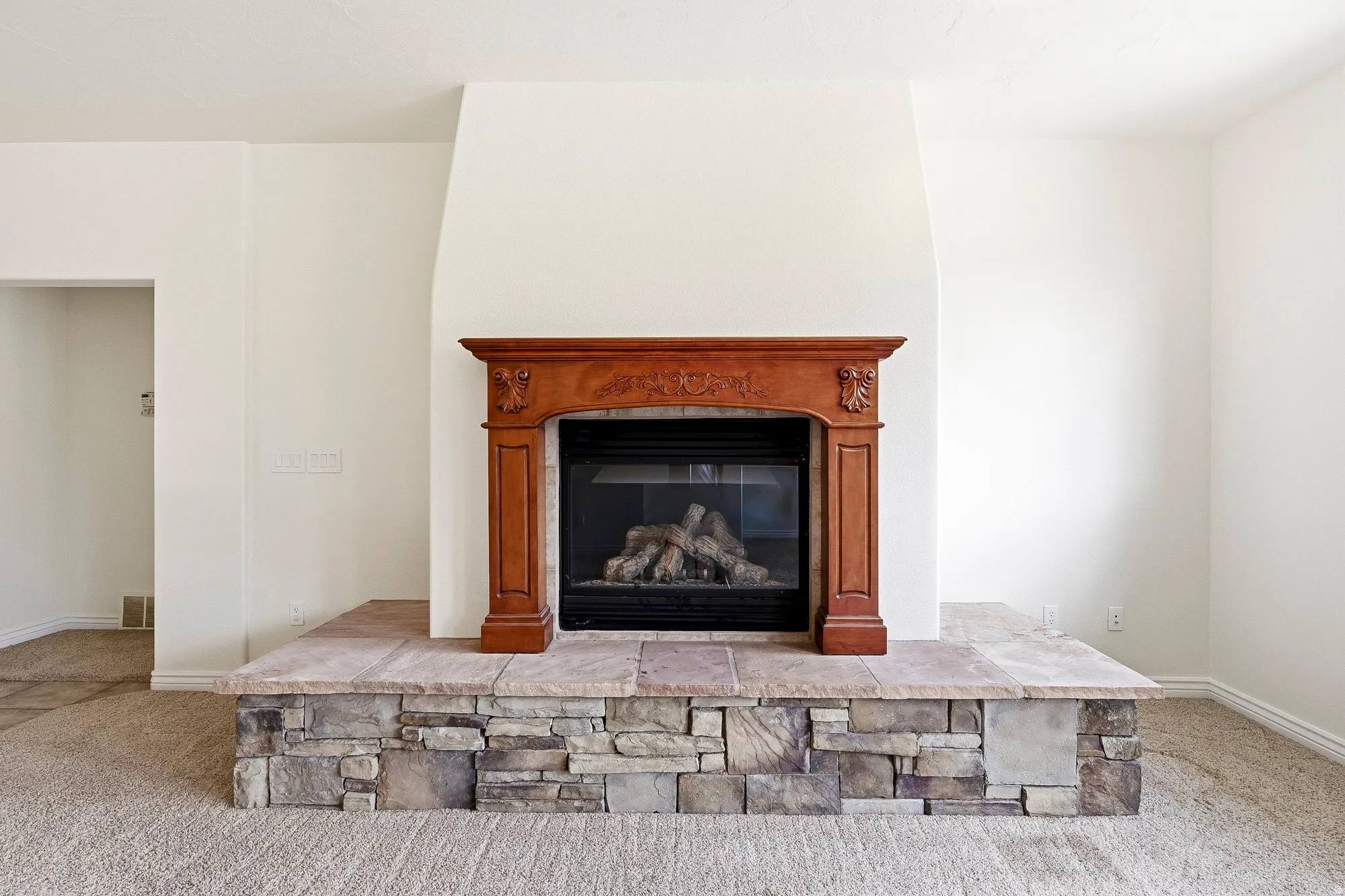 Fireplace featuring a stone-clad hearth, natural wood mantel, and gas insert