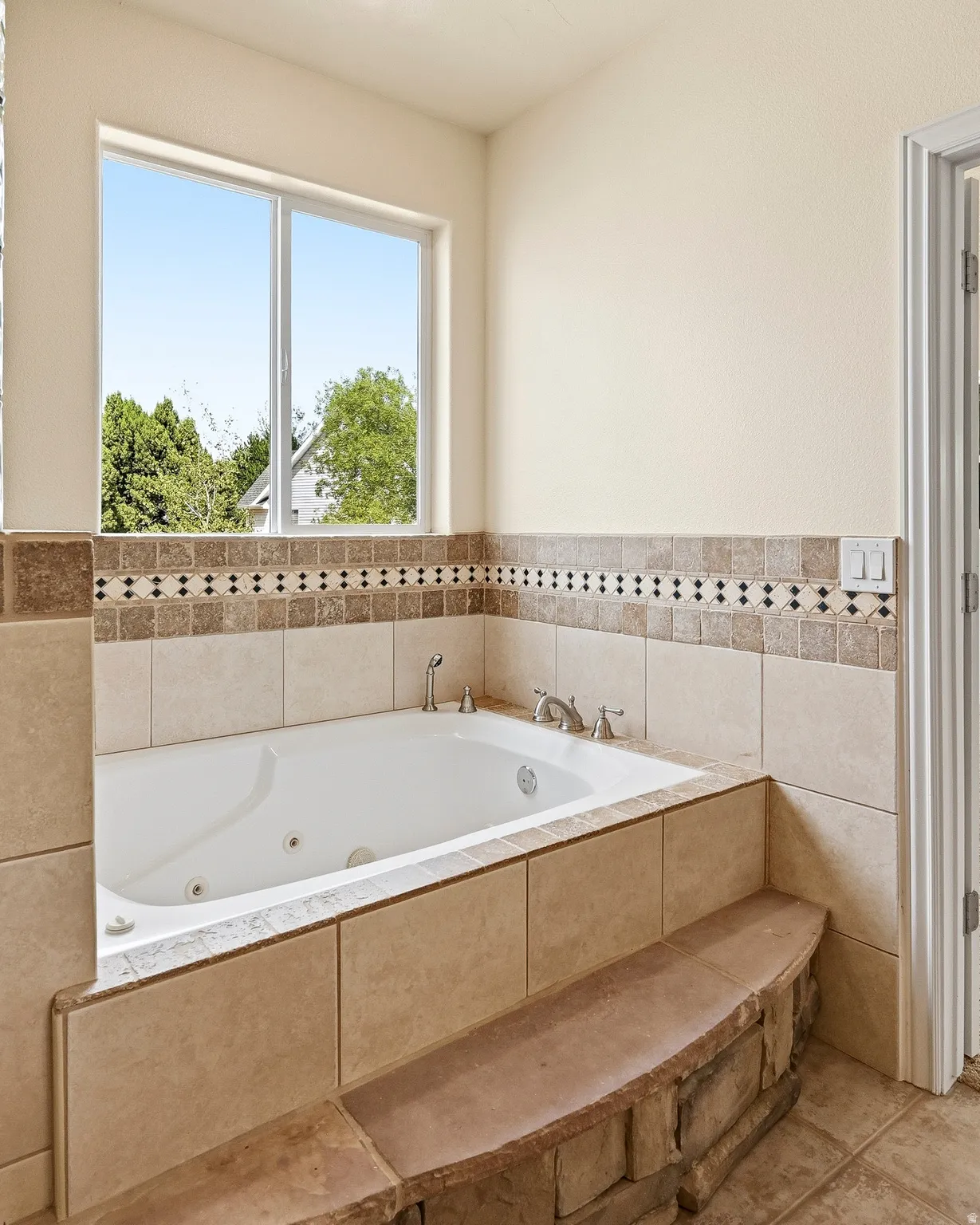 Built-in jetted tub with tile surround, decorative tile accent band, and an integrated stone-faced bench