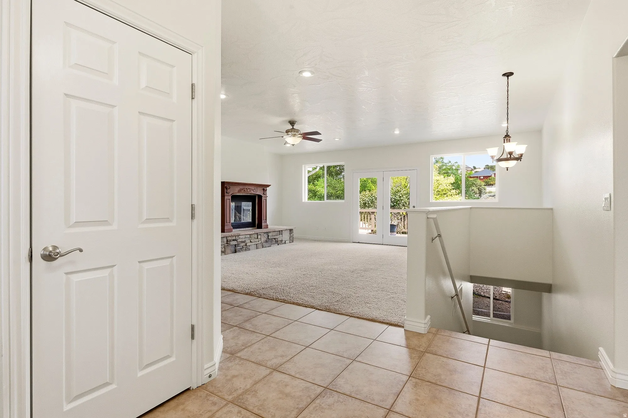 Tile flooring, a wood-finish fireplace with stone surround, recessed lighting, ceiling fan, and French doors to an outdoor deck