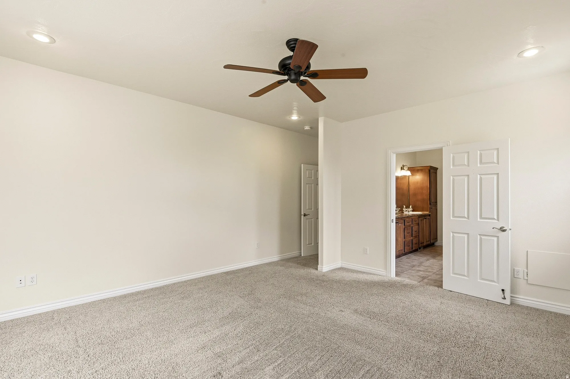 Recessed lighting, ceiling fan, neutral carpet, wood-finish vanity, and panel doors