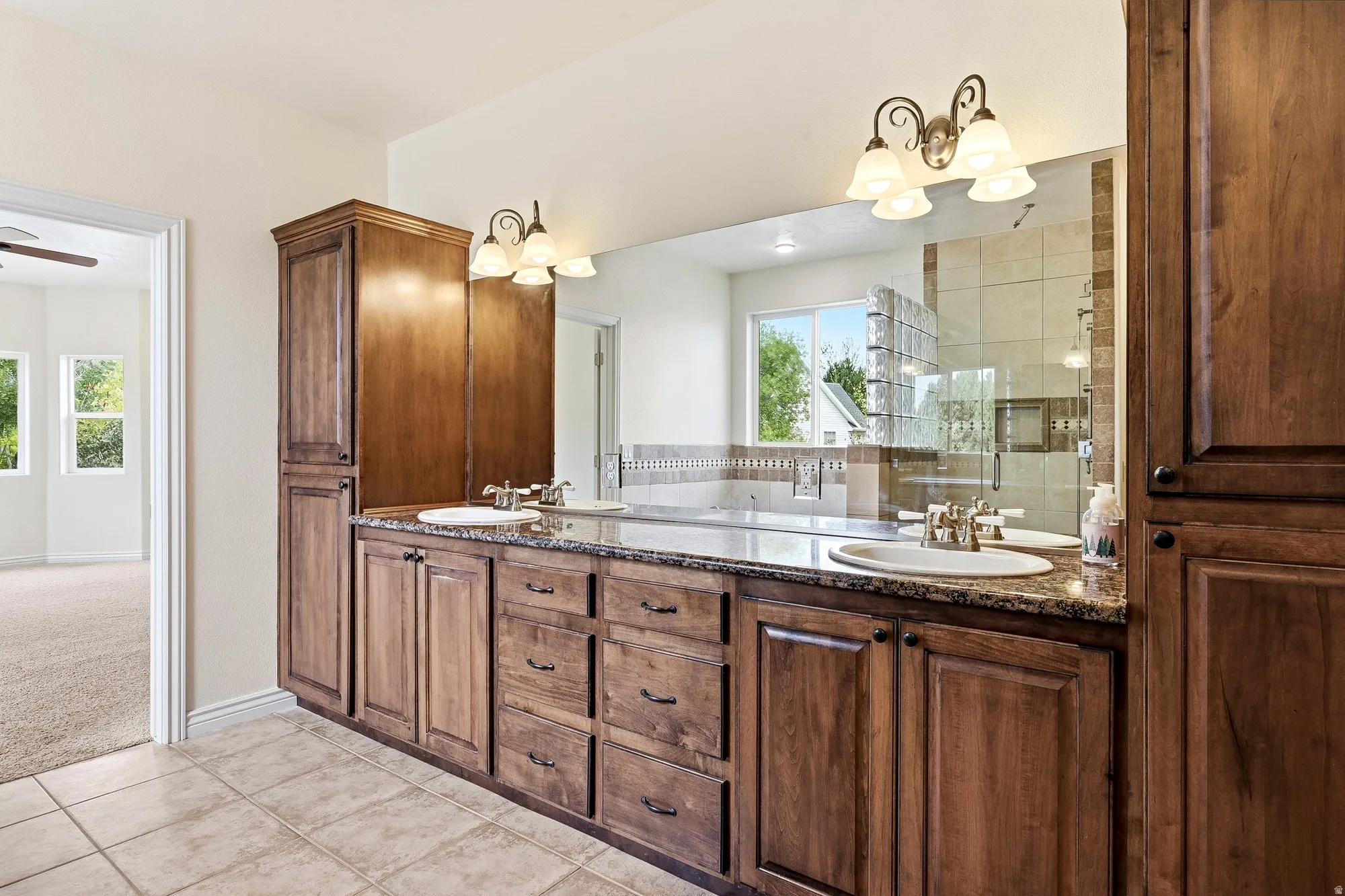 Dual vanity with integrated sinks, extensive wood cabinetry, granite-style countertop, and a large mirror