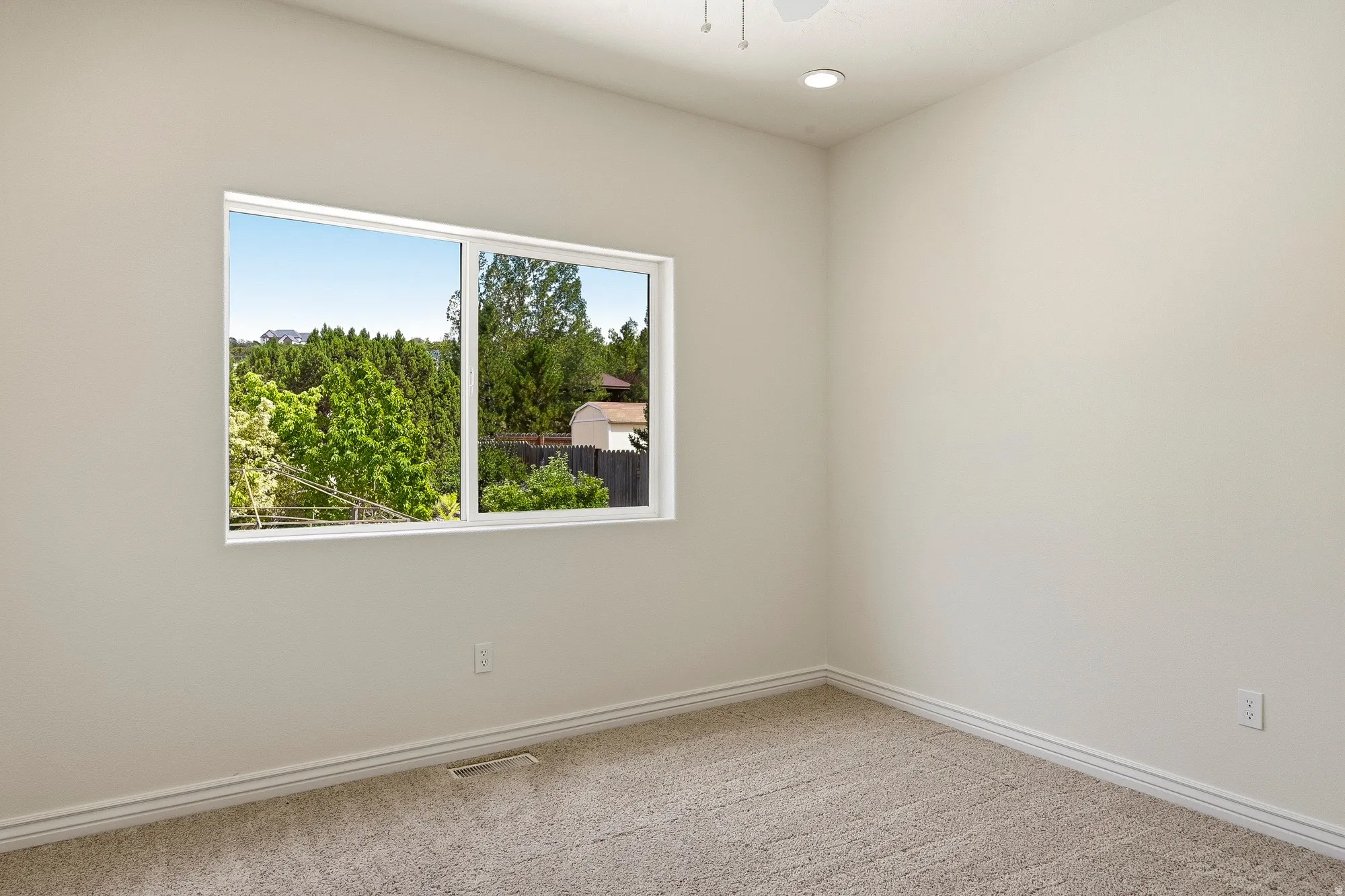 Neutral wall paint, plush carpeting, a large window, and recessed lighting