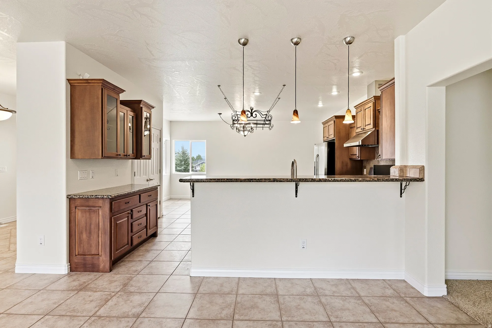 Tile flooring, wood cabinetry with glass-front uppers, granite-style countertops, bar seating, and pendant lighting