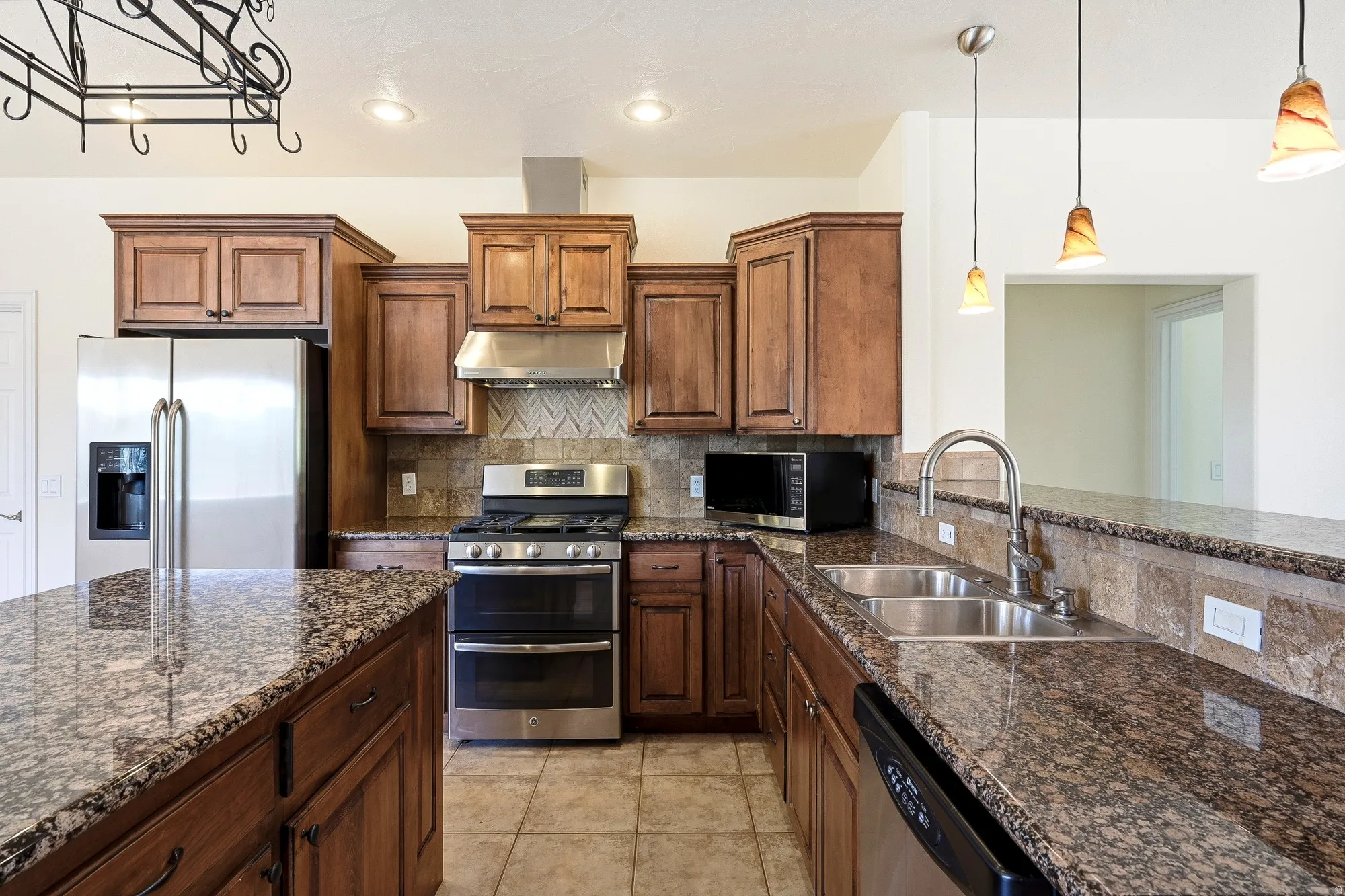 Kitchen featuring wood cabinetry, stainless steel appliances, speckled stone countertops, a tile backsplash, and recessed lighting